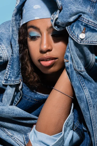 African american woman with makeup posing with denim jacket isolated on blue — Stock Photo