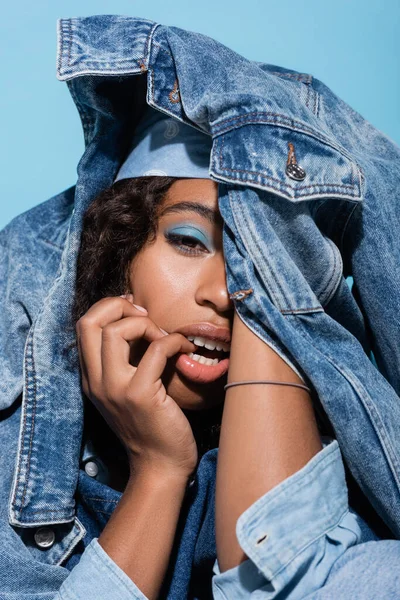 Sensual african american woman obscuring face with denim jacket isolated on blue — Fotografia de Stock