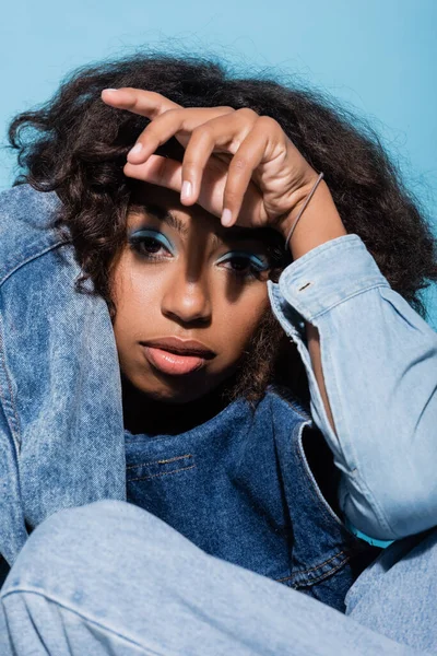 African american woman with makeup and wavy hair looking at camera isolated on blue - foto de stock