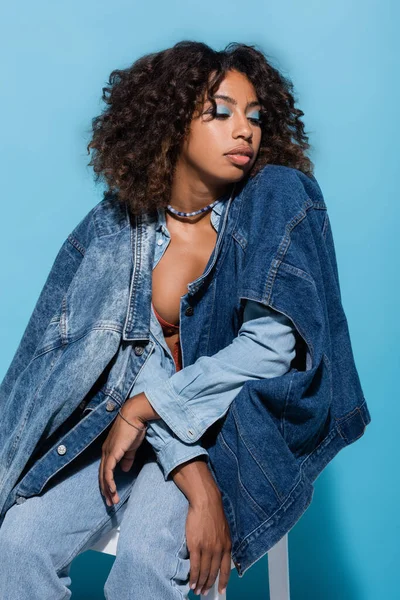 Brunette african american woman posing with denim garments on blue background — Photo de stock