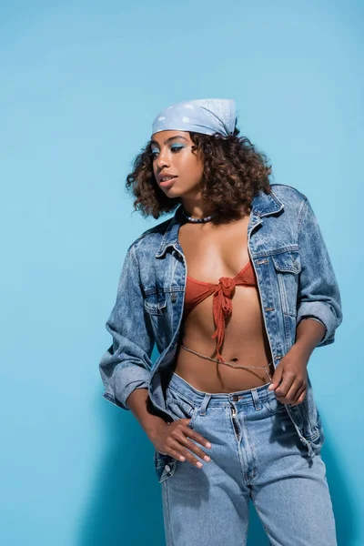 Curly african american woman in denim jacket and swim bra on blue background — Stockfoto