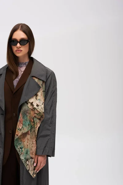 Teenage model in stylish sunglasses and trench coat isolated on grey — Fotografia de Stock