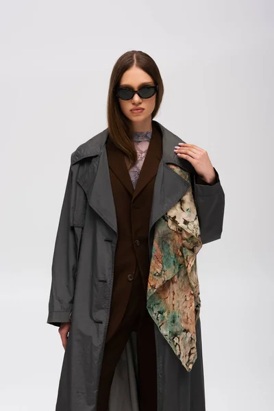 Брюнетка-подросток в стильных солнцезащитных очках и модном пальто, изолированном на сером — стоковое фото