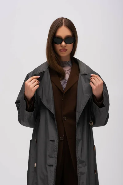 Stylish teenage girl in sunglasses and trendy trench coat posing isolated on grey — Photo de stock