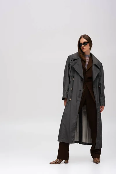 Full length of stylish teenage model in sunglasses and trendy trench coat posing on grey — Fotografia de Stock