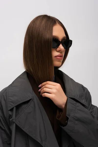 Stylish teenage model in sunglasses and trench coat posing isolated on grey — Fotografia de Stock