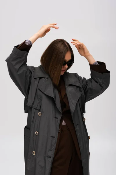 Модель-підліток в сонцезахисних окулярах і модна траншея пальто позує ізольовано на сірому — стокове фото