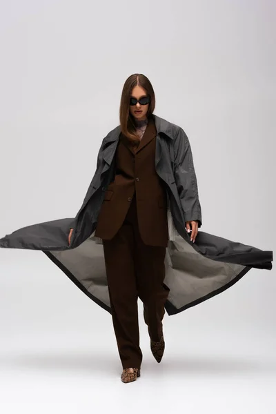 Full length of stylish teenage model in suit and trendy trench coat walking on grey — Fotografia de Stock