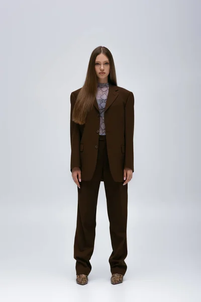 Full length of pretty teenage model in brown high-quality suit standing on grey - foto de stock