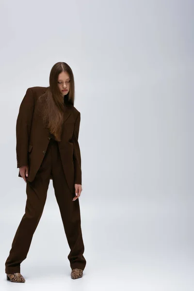 Full length of brunette teenage model in brown high-quality suit posing on grey — Stock Photo