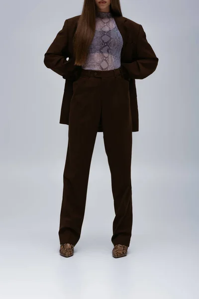 Обрізаний вид підліткової моделі в коричневому високоякісному костюмі позує на сірому — стокове фото