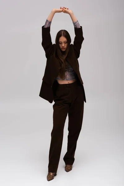 Full length of teenage model in stylish high-quality suit posing with raised hands on grey — Stock Photo