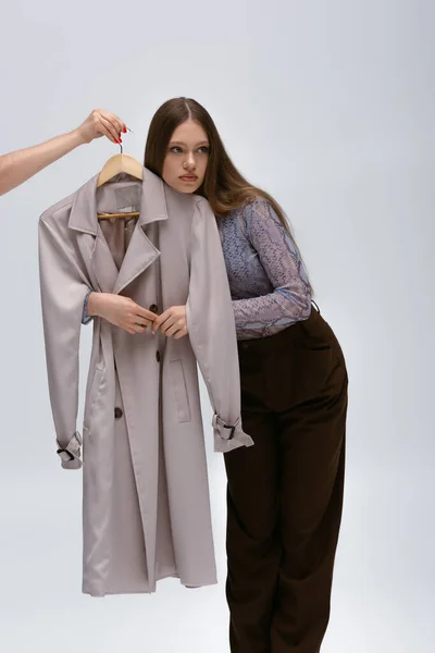 Teenage model hugging recyclable trench coat while woman holding hanger on grey — Fotografia de Stock