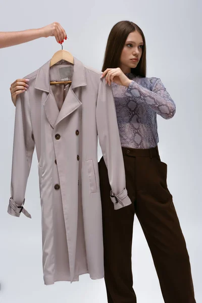 Teenage model and woman hugging stylish trench coat on hanger isolated on grey — Fotografia de Stock
