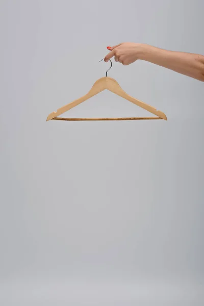 Partial view of woman holding wooden hanger isolated on gray - foto de stock