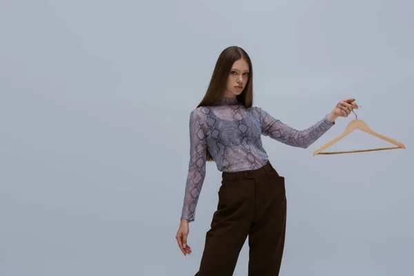 Brunette teenage girl holding wooden hanger while posing isolated on grey — Fotografia de Stock