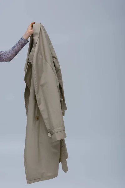 Partial view of woman holding trendy trench coat isolated on grey — Stockfoto