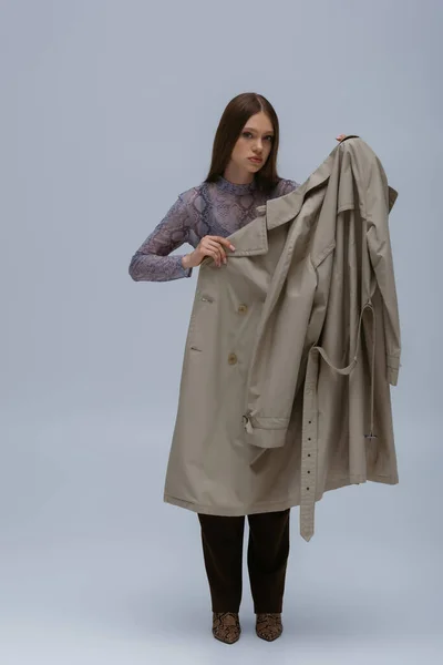Brunette teenage girl posing with trendy trench coat isolated on grey — Stock Photo
