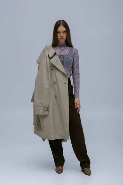 Full length of teenage model posing with stylish trench coat on grey — Stock Photo