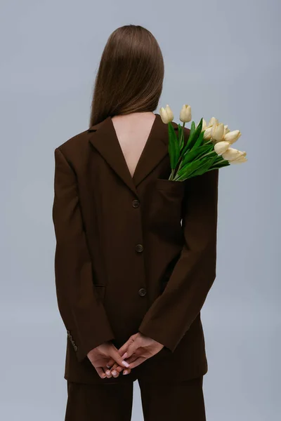 Задний вид модели подростка в коричневом блейзере с букетом тюльпанов, изолированных на сером — стоковое фото