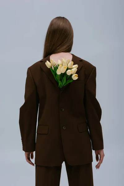 Back view of teenage model in brown blazer with tulips isolated on grey — Stock Photo