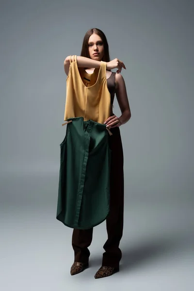 Full length of brunette model holding clothing with clothespins on grey — Stock Photo