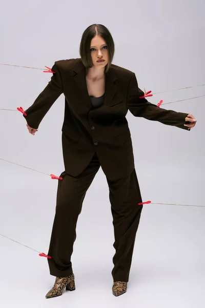 Full length of stylish teenage girl in brown suit pinned with clothespins on rope posing on grey — Fotografia de Stock