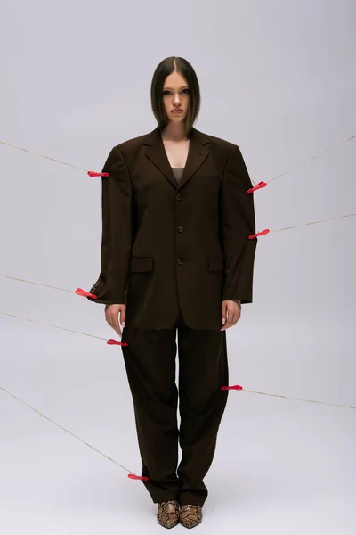 Full length of teenage girl in brown stylish suit pinned with clothespins on rope posing on grey — Foto stock