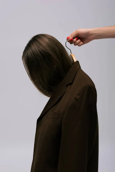Женщина, держащая вешалку с коричневой моделью в коричневом пиджаке, изолированном на сером — стоковое фото