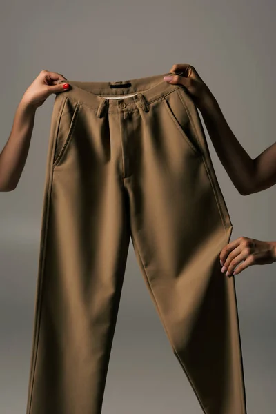 Cropped view of women holding recyclable beige pants isolated on grey — Foto stock