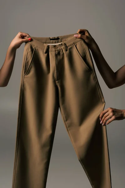 Cropped view of women holding recyclable beige pants isolated on grey - foto de stock