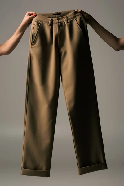 Cropped view of women holding recyclable beige pants on grey — Stock Photo