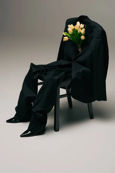 Bouquet of tulips and blue stylish suit hanging on chair on grey — Photo de stock