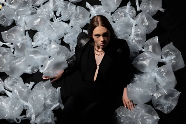 Top view of brunette model in stylish suit posing around plastic bags on black — Foto stock