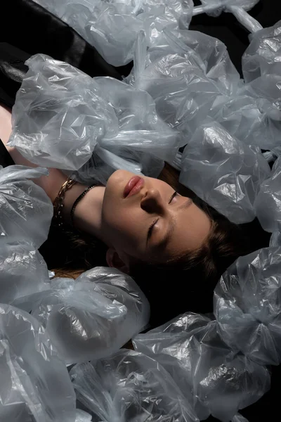 Над головой вид брюнетки модели с закрытыми глазами лежащих вокруг пластиковых пакетов, переработка концепции моды — стоковое фото
