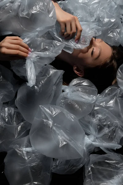 Top view of model with closed eyes lying around plastic bags, recycle fashion concept — Stockfoto