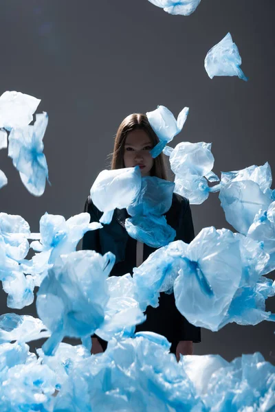 Brunette model in suit posing near flying blue plastic bags on dark grey — Photo de stock