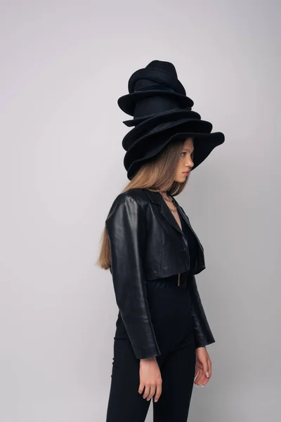 Side view of brunette model in leather jacket and different black hats on head isolated on grey - foto de stock
