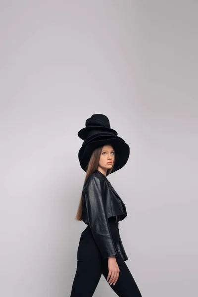Брюнетка модель в шкіряній куртці і чорні капелюхи на голові ізольовані на сірому — стокове фото