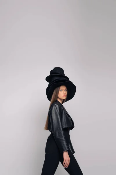 Brunette model in leather jacket and black hats on head isolated on grey — Stock Photo