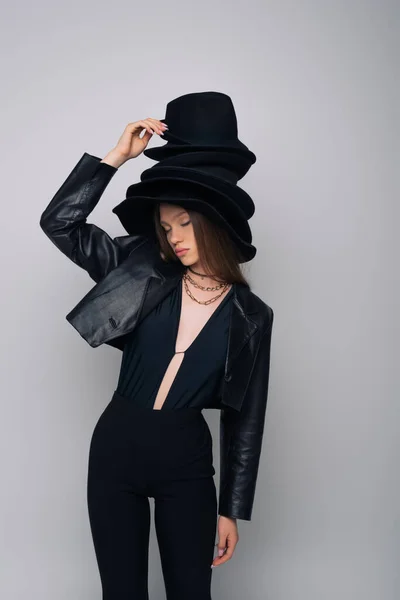 Brunette model in leather jacket holding derby hat isolated on grey - foto de stock