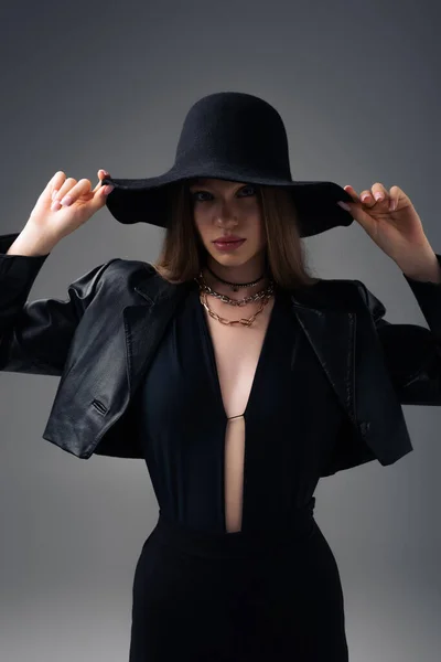 Teenage model in leather jacket adjusting floppy hat isolated on grey — Photo de stock