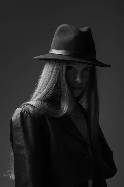 Monochrome photo of teenage model in fedora hat looking at camera in studio - foto de stock