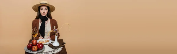 Woman in straw hat sitting near food and wine on table isolated on beige, banner — Foto stock