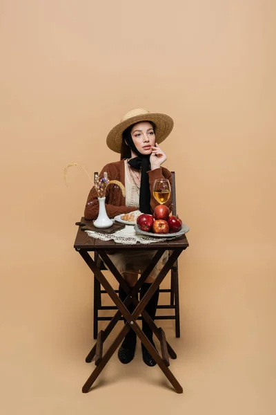 Stylish woman posing near wine and food on table on beige background — Stockfoto