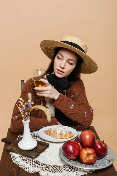 Trendy woman holding wine near apples and croissant on table isolated on beige — Photo de stock