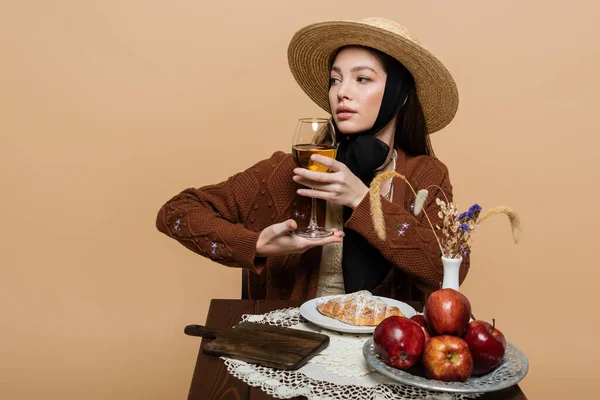 Молода стильна жінка позує зі склянкою вина біля їжі на столі ізольована на бежевому — стокове фото