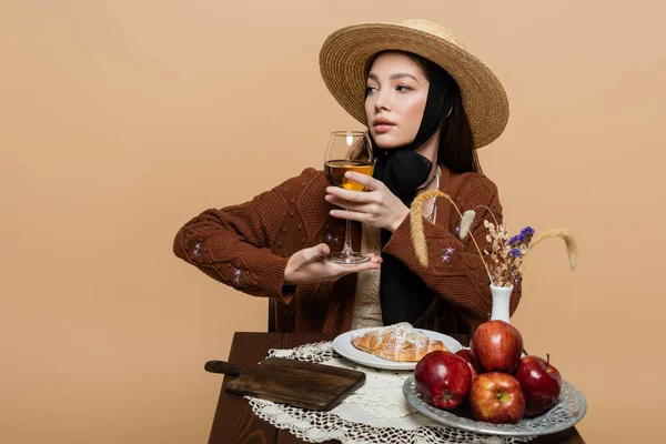 Young stylish woman posing with glass of wine near food on table isolated on beige — Stock Photo