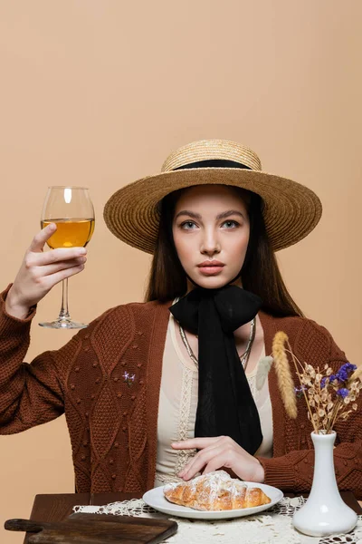 Young woman in sun hat holding glass of wine near food and plants isolated on beige - foto de stock