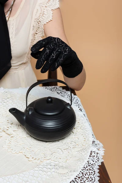 Обрезанный вид стильной женщины в перчатках сидя рядом чайник на столе изолированы на бежевый — стоковое фото